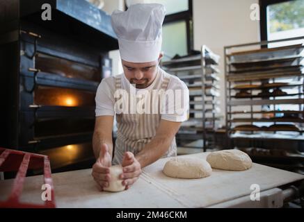 Junger Bäcker mit Down-Syndrom, der Gebäck in der Bäckerei herstellt. Konzept der gesellschaftlichen Integration von Menschen mit Behinderungen. Stockfoto