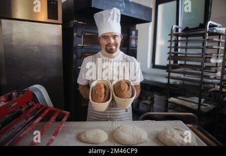 Junger Bäcker mit Down-Syndrom, der Gebäck in der Bäckerei herstellt. Konzept der gesellschaftlichen Integration von Menschen mit Behinderungen. Stockfoto