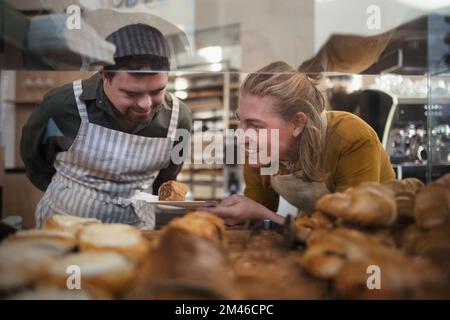 Ein Mann mit Down syndrom, der seinem Kollegen in einem Café hilft. Konzept der gesellschaftlichen Integration von Menschen mit Behinderungen. Stockfoto