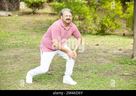 Indischer Senior-Mann mit Knieschmerzen. Asiatischer alter Mann verletzte sich beim Laufen im Park sein Bein. Stockfoto