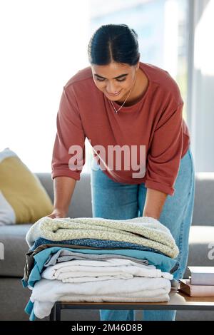 Frau, falte Wäsche und Tisch zu Hause mit sauberem Handtuch, Stoff oder ordentlich für Gastfreundschaft mit Lächeln. Viel Spaß beim Reiniger, Baumwolle und Textilien in der Lounge Stockfoto