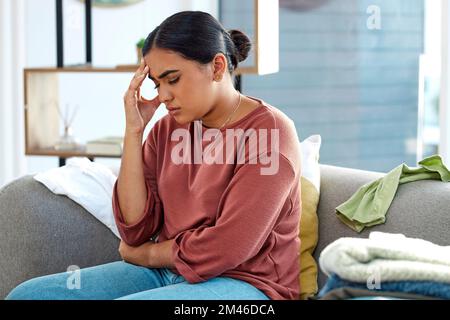 Stress, Frau und Kopfschmerzen auf dem Sofa, Depressionen und psychische Gesundheit in der Lounge. Weiblicher Kopf, Angst und Burnout im Wohnzimmer, leiden an Stockfoto