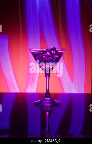 Martini-Glas mit Eis, auf der Bar. Vor dem Hintergrund von Neonlicht. Stockfoto