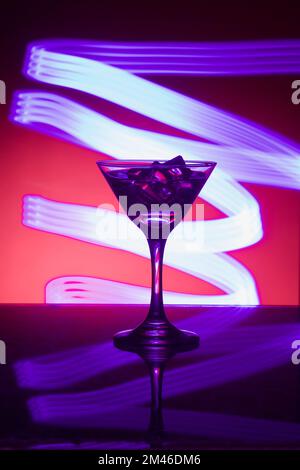 Martini-Glas mit Eis, auf der Bar. Vor dem Hintergrund von Neonlicht. Stockfoto