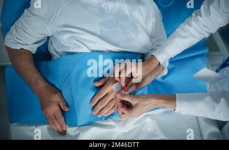 Draufsicht der Krankenschwester beim Anbringen der Kanüle an der Hand des Patienten. Stockfoto