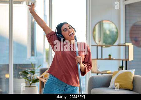 Reinigung, Gesang und Frau tanzen zu Musik für Spaß, Energie und Glück, während sie die Zimmerreinigung, Wischmopp und Besen im Wohnzimmer macht. Frühjahrsputz Stockfoto