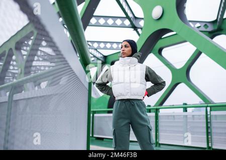 Junge muslimische Frau, die sich nach dem Joggen ausruht, draußen in der Stadt. Stockfoto