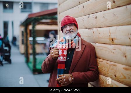 Glücklicher Seniorenmann genießt den weihnachtsmarkt, trinkt Glühwein. Stockfoto