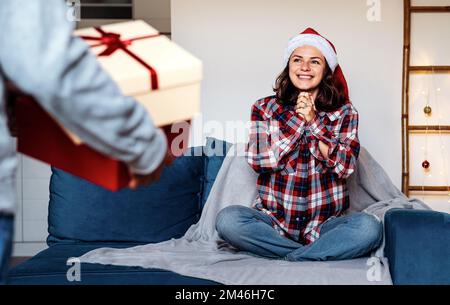 Eine junge Frau mit Weihnachtsmannmütze, die Weihnachten von ihrem Freund bekommt. Stockfoto