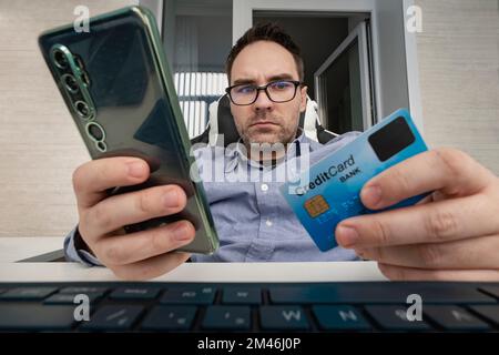 Ein Geschäftsmann hält seine Kreditkarte und kauft von zu Hause aus online ein, mit Laptop, E-Commerce für Zahlungen, Internet-Banking, Geld für den Urlaub ausgeben. Mann Stockfoto