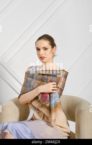 Junge Frau mit Seidenschal auf den Schultern, die im Sessel posiert Stockfoto