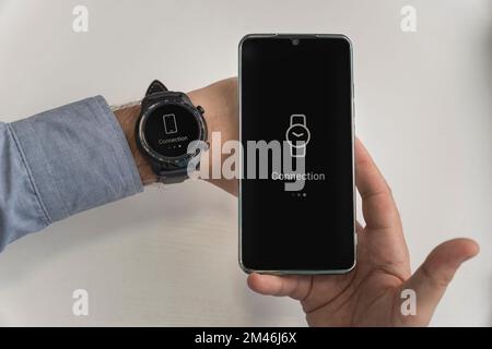 Ein Mann hält ein Smartphone und eine Smartwatch in der Hand. Kabellose Verbindung von Uhr und Mobiltelefon. Wi-Fi-Anschluss für Smartphone und Smartwatch Stockfoto