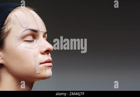 Gesichtskinesiologisches Klebeband auf weiblichem Gesicht in Nahaufnahme. Stockfoto