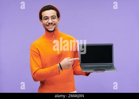 Junger erfolgreicher Programmierer, der auf einen leeren Bildschirm des Laptops zeigt, während er neue Software präsentiert und in die Kamera schaut Stockfoto