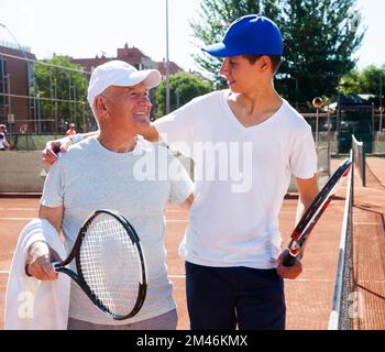 Großvater und Enkel sprechen auf dem Tennisplatz und spielen Tennis Stockfoto