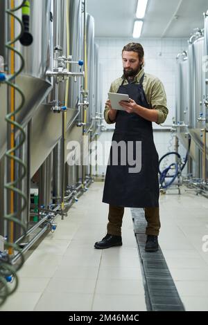 Besitzer einer Bierbrauerei, die den Produktionsprozess über die Anwendung auf einem digitalen Tablet steuert Stockfoto