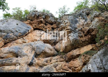 Herrlicher Blick auf graubraune Felsen von unten mit einigen Grünflächen auf dem Gipfel der Klippe Stockfoto