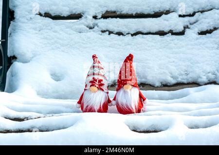 Weihnachtskarte süße skandinavische Zwerge mit rotem Hut und weißem Bart auf verschneiter Winterbank Märchen Schneefall Winterzeit Hallo Dezember, Janua Stockfoto