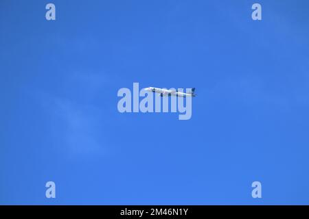 Entferntes Passagierjet-Flugzeug, das in großer Höhe am blauen Himmel fliegt. Stockfoto