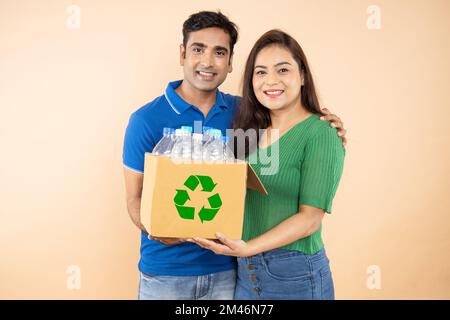 Glückliches, umweltfreundliches, junges indisches Paar, das eine Schachtel voller Plastikflaschen hält, um sie zu recyceln. Umweltschutz, Earth-Day-Konzept Stockfoto