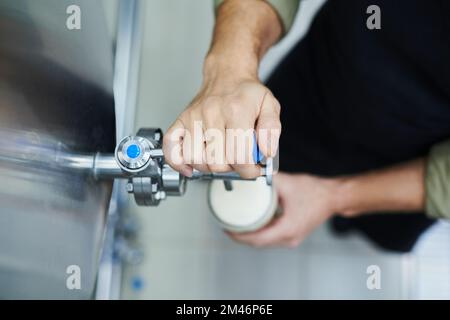 Nahaufnahme eines Brauereiarbeiters, der Bier aus dem Tank in großes Glas gießt Stockfoto