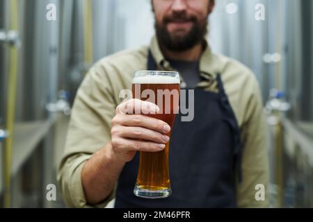 Abgeschnittenes Bild des Eigentümers einer Mikrobrauerei mit einem großen Glas Bier Stockfoto