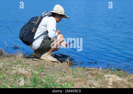 Umweltschützerin mit Mobiltelefon zur Erfassung der Analyse von Krankheitserregern in natürlichen Gewässern. Wasser- und Ökologiekonzept Stockfoto