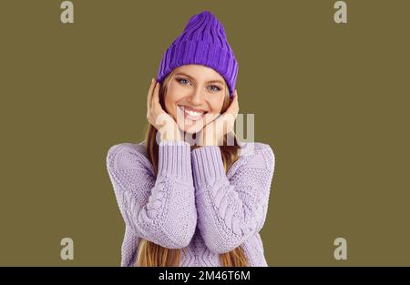 Porträt einer glücklichen, wunderschönen jungen Frau mit warmem lila Winterhut und Pullover Stockfoto