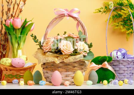 Osterkomposition. Korb mit Blumen und Eiern Spielzeugkaninchen auf dem Tisch. Stockfoto