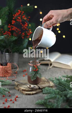 Heiße Schokolade im Glasgefäß mit Tanne und roten Beeren auf festlichem rustikalem Hintergrund. Stockfoto