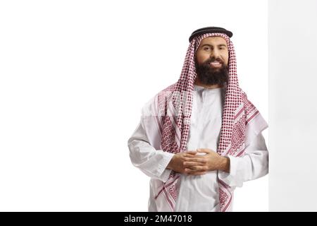 Saudi-arabischer Mann, der ein traditionelles Gebäude trägt und sich an eine Wand lehnt, isoliert auf weißem Hintergrund Stockfoto
