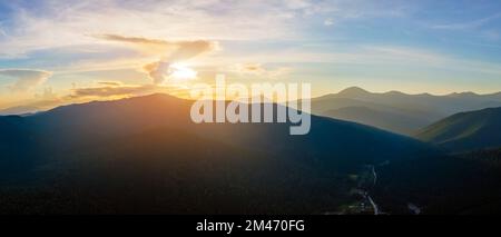 Luftaufnahme der dunklen Berge mit hellen Sonnenstrahlen der untergehenden Sonne bei Sonnenuntergang. Am Abend dunstigen Gipfeln und nebligen Tälern Stockfoto