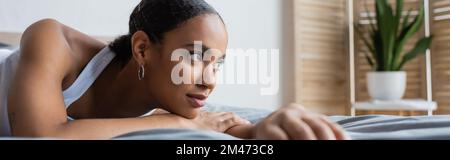 Junge afroamerikanische Frau, die auf dem Bett liegt und wegschaut, Banner, Börsenbild Stockfoto