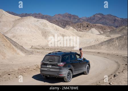 Ein junges Mädchen, das einen schwarzen Ford Escape SUV durch die Wüste des Death Valley fährt, Urlaub Stockfoto