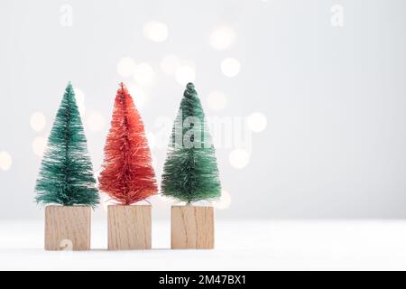 Drei niedliche Weihnachtsminiatur-Tannen auf einem weißen Tisch mit Bokeh-Lichtern Horizontal mit Kopierbereich Stockfoto