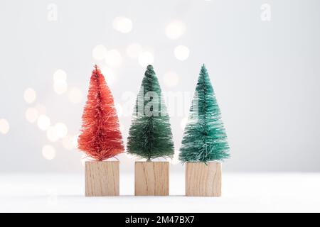 Drei niedliche Weihnachtsminiatur-Tannen auf einem weißen Tisch mit Bokeh-Lichtern Horizontal mit Kopierbereich Stockfoto