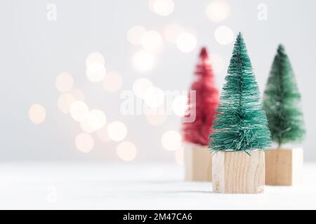 Drei niedliche Weihnachtsminiatur-Tannen auf einem weißen Tisch mit Bokeh-Lichtern Horizontal mit Kopierbereich Stockfoto