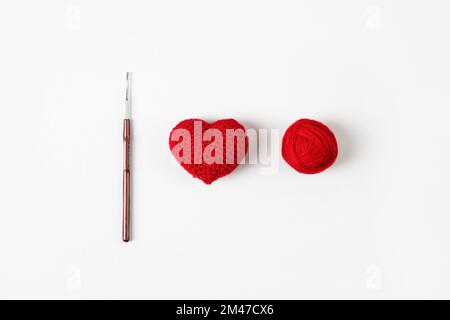 Gekröpftes rotes Herz auf grauem Hintergrund und ein Fadenball mit einem Haken. Valentinstag, Symbol der Liebe. Stockfoto