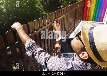 Mann mit Strohhut und Sonnenbrille, der sich im Sommer auf dem Balkon entspannen kann. Stockfoto