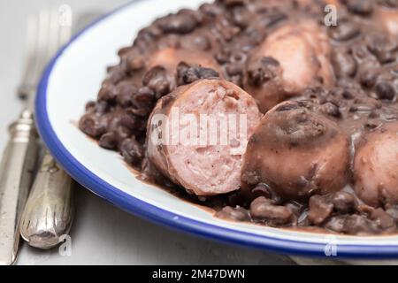 Eintopf aus schwarzen Bohnen mit Würstchen auf einem weißen Gericht Stockfoto