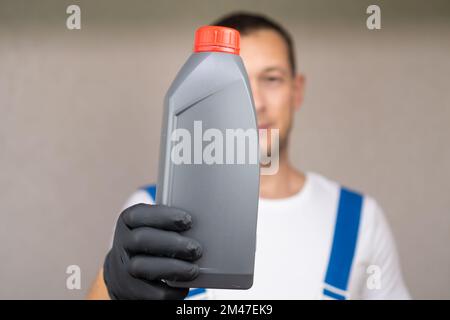 Automechaniker in einem weißen T-Shirt und blauem Overall hält eine Flasche Motoröl vor sich und schaut in die Kamera, Kopierraum. Stockfoto