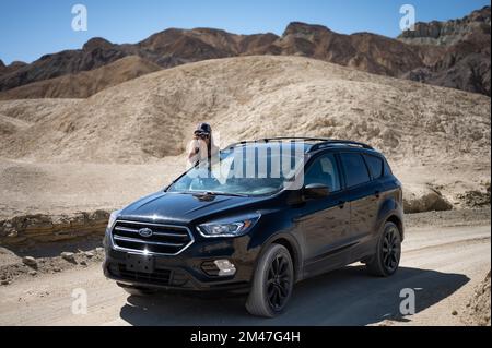 Abenteuerlustiges junges Mädchen, das einen schwarzen Ford Escape SUV durch die Wüste fährt Stockfoto
