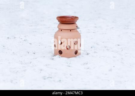 Im Winter gibt es einen Tontopf im Garten. Es ist ein kleiner Keramikkamin aus Ton. Eine Kerze darin erhitzt eine Schüssel Wasser für Wildvögel. Die dr. Stockfoto