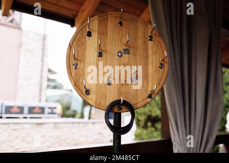 Stahlhaken mit Nummern für Kleidung auf einem runden Holzbrett im Restaurant, Café. Handgefertigt. Rustikaler Hintergrund Stockfoto