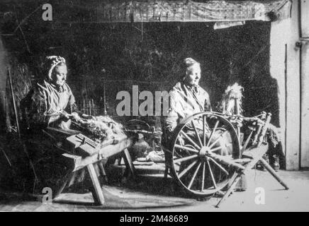 Foto aus dem frühen 20.. Jahrhundert, auf dem zwei alte weibliche Heimspinner gezeigt werden, die mit einem drehenden Holzrad und einem Hacken/Hacken zum Dressen von Flachs arbeiten Stockfoto