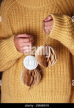 Handgemachte weihnachtliche Wabenkugeln aus weißem und braunem Kaffeefilter in Frauenhänden. Skandinavisches Handwerkspapier Konzept. Selektiver Fokus. Stockfoto