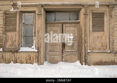 Türen und Fenster eines sehr alten Hauses. Schnee vor dem Haus. Im Winter. Stockfoto