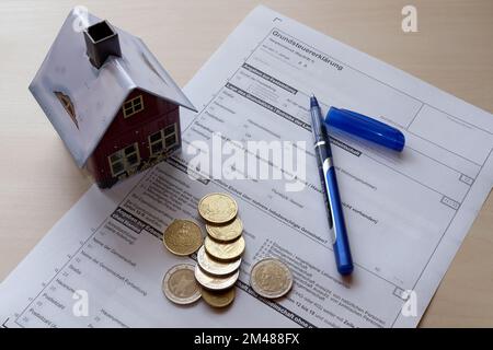 Symbol-Image-Vermögenssteuerreform: Steuererklärung mit Haus, Stift und Münzen. Stockfoto