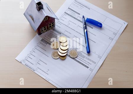 Symbol-Image-Vermögenssteuerreform: Steuererklärung mit Haus, Stift und Münzen. Stockfoto