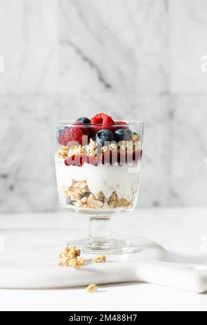Ein mehrschichtiges Dessert aus Müsli, Joghurt, Marmelade und frischen Beeren in einem Servierglas Stockfoto